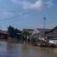Luapan Kali Cikarang Bekasi Laut lumpuhkan akses jalan. Warga gunakan gerobak untuk bantu sesama melintas genangan.
